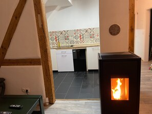 Une cuisine moderne avec un mur recouvert de carreaux, une cuisinière noire dont la flamme est visible et un plafond en bois.