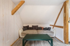 Et loftrum med træbjælker i loftet, en hvid væg, en beige sofa med puder og et grønt bord.