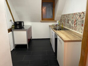 Una cocina pequeña con ventana, cafetera, lavamanos y azulejos con diseño.