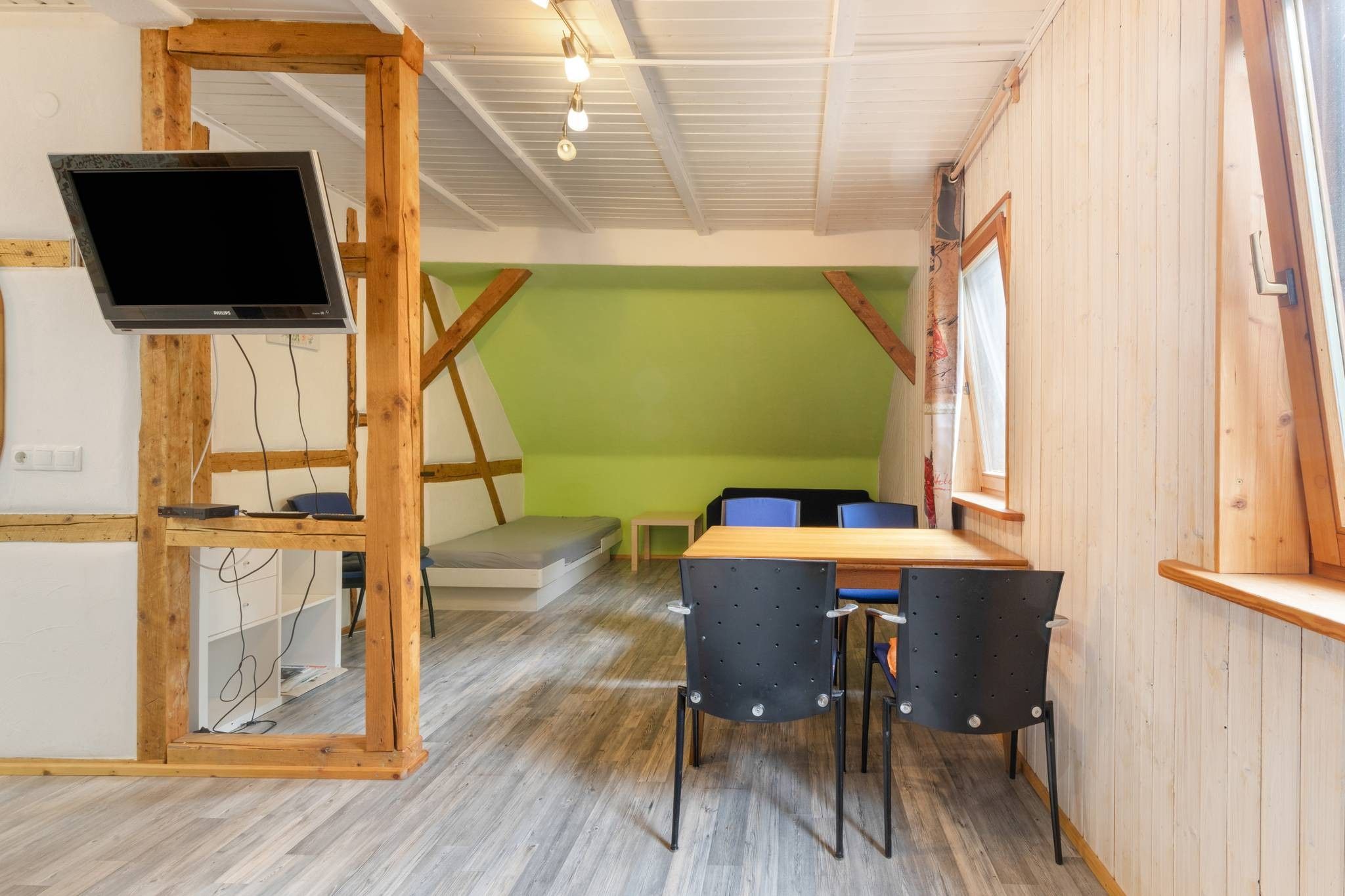Een kamer met een houten tv-meubel, een tafel met stoelen, een groene muur en een raam.