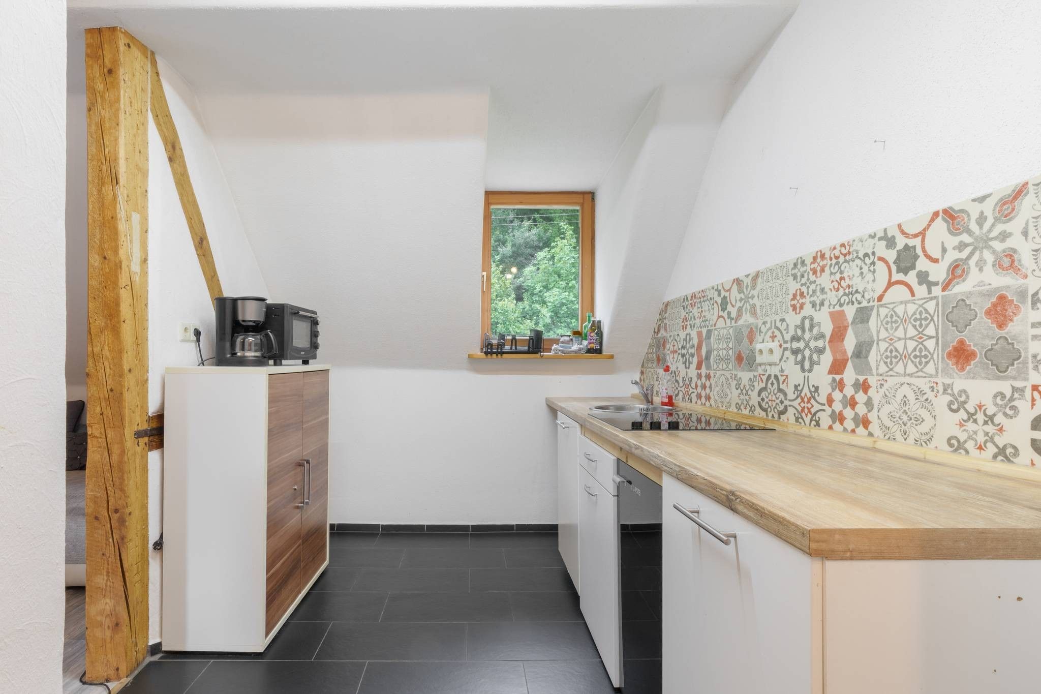 Een kleine keuken met een houten balk, een raam met uitzicht en een betegelde achterwand.