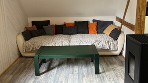 A loft-style room with a wooden beam ceiling, a sofa with patterned cushions, a green bench, and a black entertainment unit.