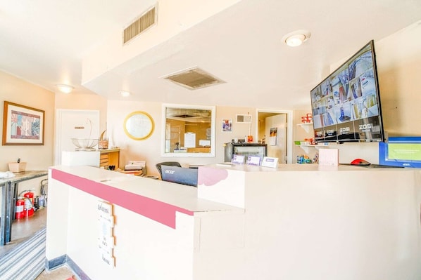 A reception area with a counter, a computer monitor, a fire extinguisher, and a wall-mounted clock.