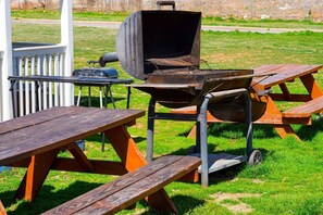 A barbecue grill with a table and benches in a grassy outdoor area.