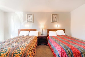 A hotel room with two beds, a nightstand, a lamp, and framed pictures on the wall.