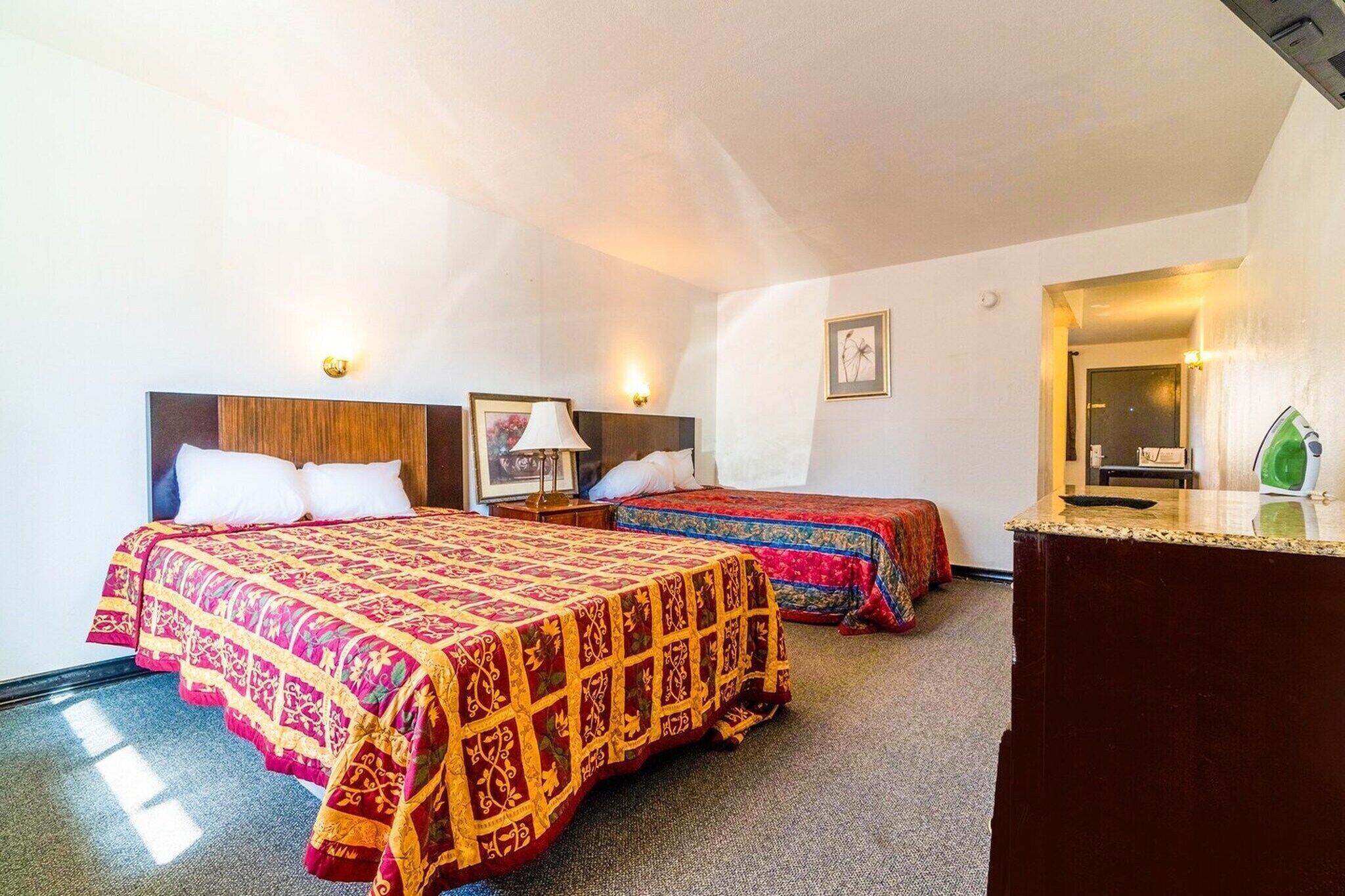 A hotel room with two beds, a desk, a mirror, and a small kitchenette.