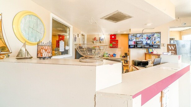 Una zona de recepción con un reloj, un perchero metálico y un televisor que muestra varias pantallas.