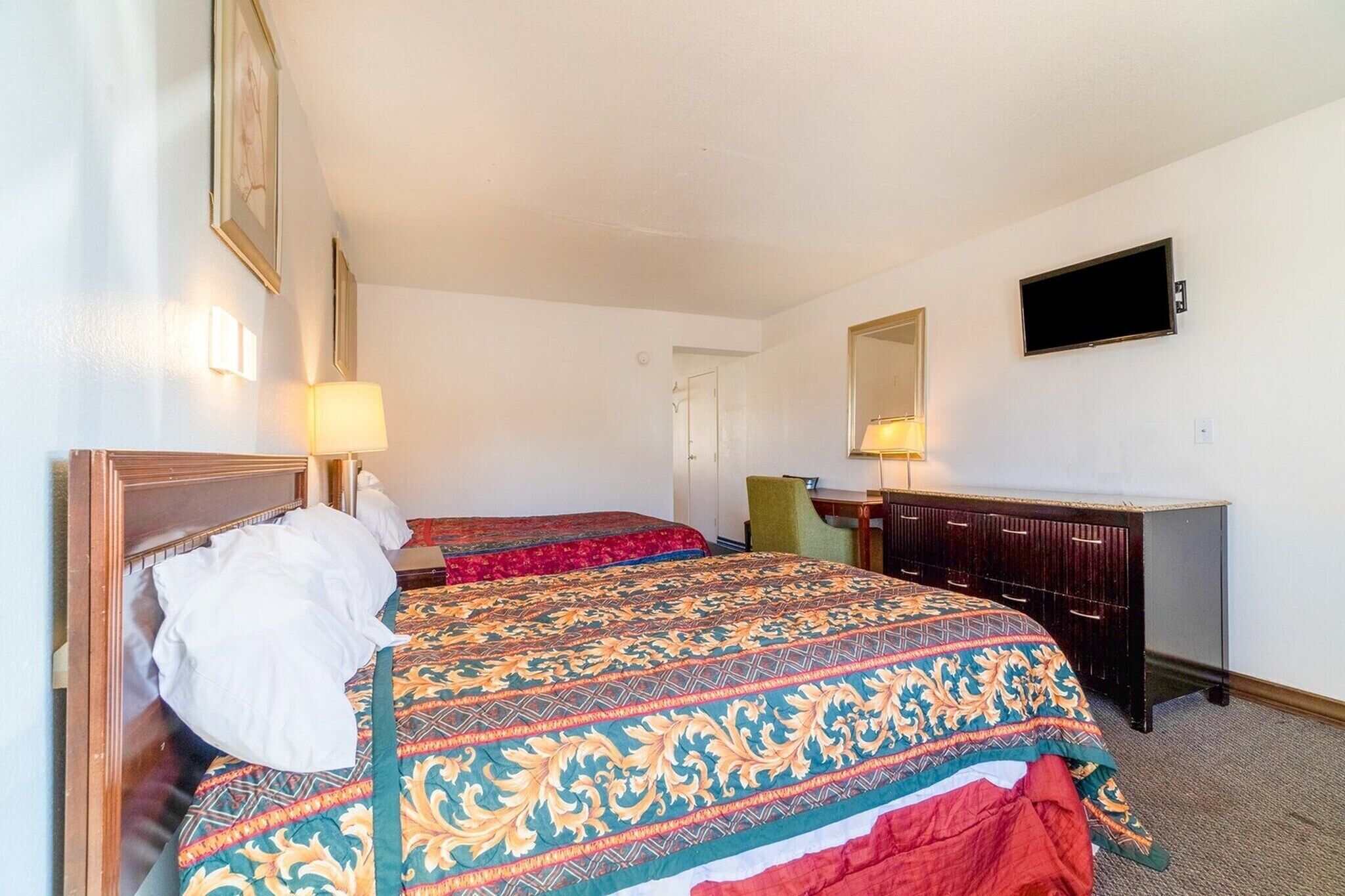Une chambre d’hôtel avec deux lits, un bureau, une chaise, une télévision et un miroir au mur.