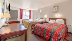 Habitación de hotel con dos camas, un escritorio, un televisor y una ventana con cortinas.