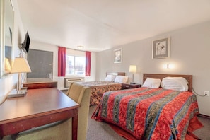 Quarto de hotel com duas camas, uma escrivaninha, televisão e janela com cortinas.