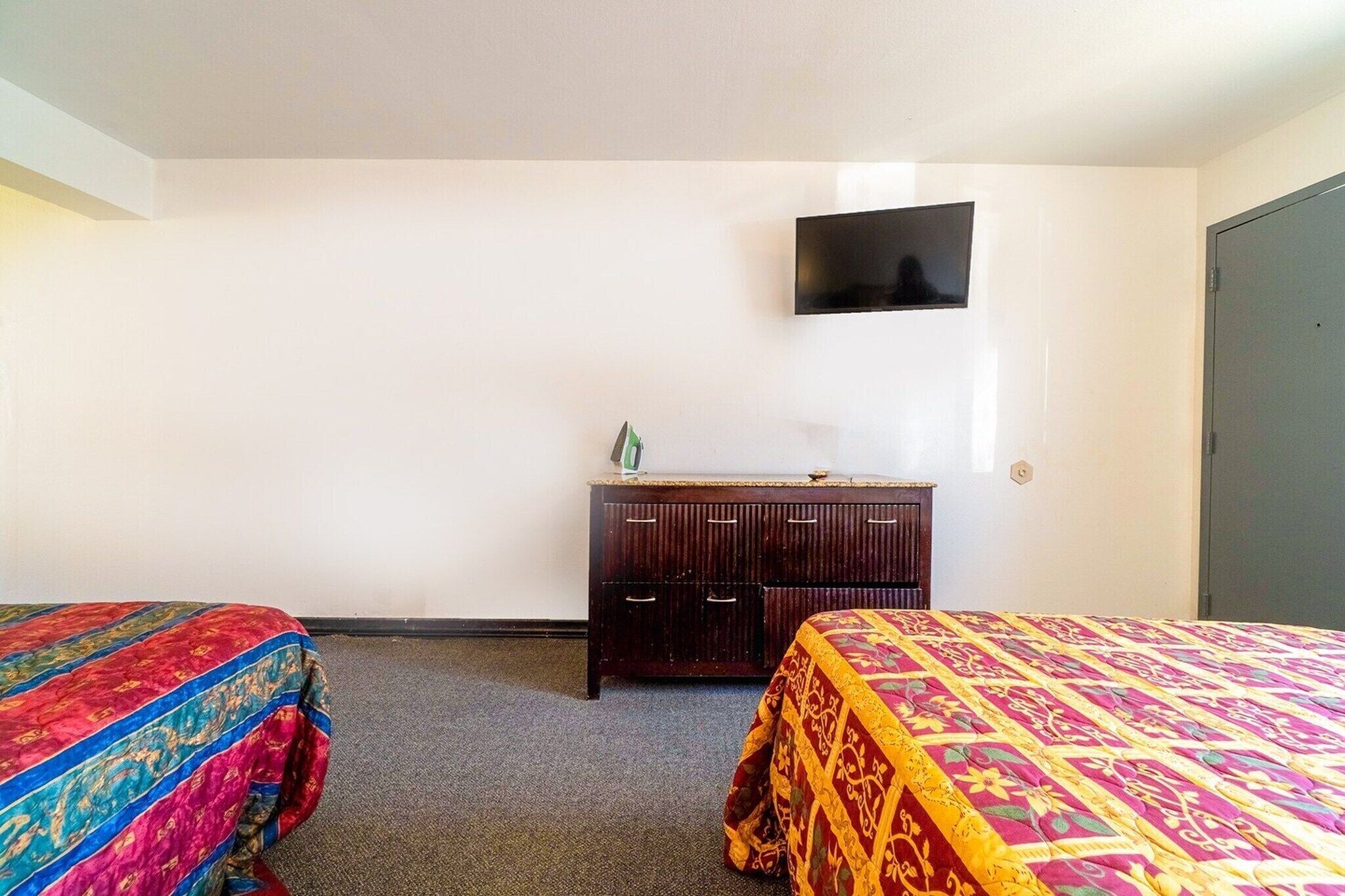 A hotel room with two beds, a dresser, a flat-screen TV, and a door.