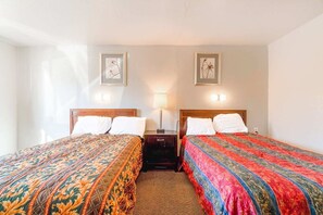 Una habitación de hotel con dos camas, una mesita de noche, una lámpara y cuadros en la pared.
