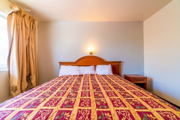 A bed with a patterned bedspread, a wooden headboard, a bedside table, and a nightstand.