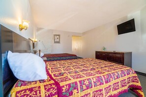 A hotel room with a bed, bedside lamp, wall-mounted TV, and a dresser.