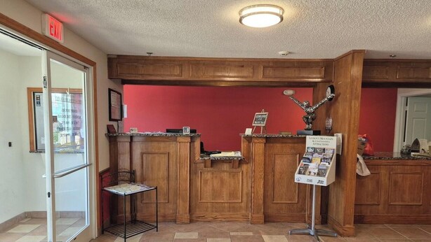 A reception area with a wooden counter, a glass door entrance, a bulletin board, and a sign about mountain attractions. - King Bed Accessible Non-Smoking (Chickamauga)