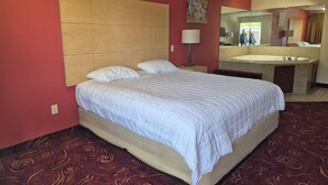 A hotel room with a large bed, a bedside table, a mirror, and a bathroom with a bathtub. - King Bed Accessible Non-Smoking (Chickamauga)