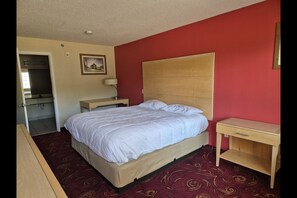 A hotel room with a bed, a desk, a chair, a mirror, and a picture on the wall.