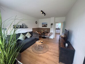Ein Wohnzimmer mit einer Couch, einem Couchtisch und einer TV-Konsole. Es gibt einen Essbereich mit einem Tisch und Stühlen.