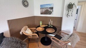 A corner seating area with a round table, wicker chairs, a wall-mounted clock, a framed picture, and a hanging plant. - Felicitas Maris - Happiness on the Baltic Sea in Dahme! (Dahme)