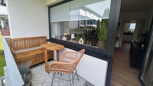 A balcony with a wooden bench, wicker chair, and a small table. - Felicitas Maris - Happiness on the Baltic Sea in Dahme! (Dahme)