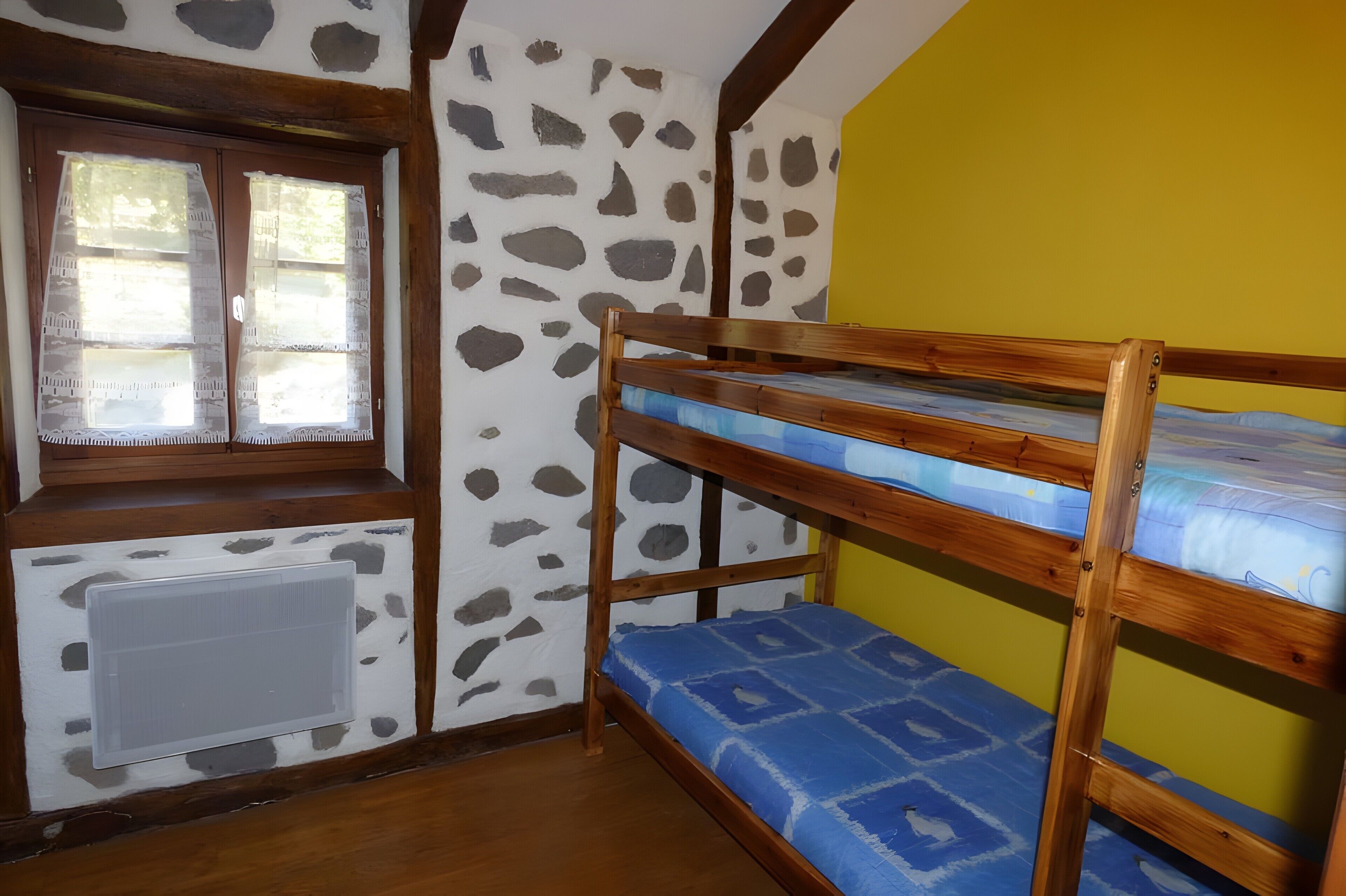 Una habitación con literas, una ventana con cortinas de encaje, un radiador y una pared con diseño de piedra.