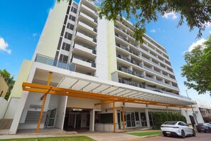 A multi-story hotel with a covered entrance, a car parked in front, and a clear sky. - Sahara Oasis - Rooftop Pool, CBD & Sunset Balcony (Darwin City)