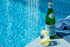 Eine Flasche S.Pellegrino Mineralwasser, ein Glas mit einer Limettenscheibe und ein blaues Handtuch am Pool.