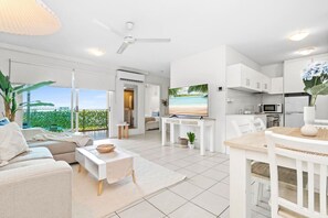 A modern, white-themed living room with a TV, sofa, and dining area. - Bluewater Retreat | Ocean-Sunset Views, Pool & CBD (Darwin City)