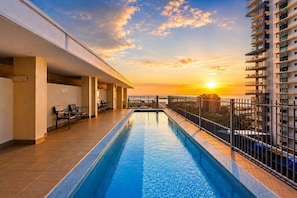 A swimming pool with a sunset view, a covered seating area, and a high-rise building in the background. - Bluewater Retreat | Ocean-Sunset Views, Pool & CBD (Darwin City)