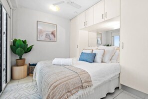 A bedroom with a bed, a potted plant, a framed picture, and a ceiling fan. - Bluewater Retreat | Ocean-Sunset Views, Pool & CBD (Darwin City)
