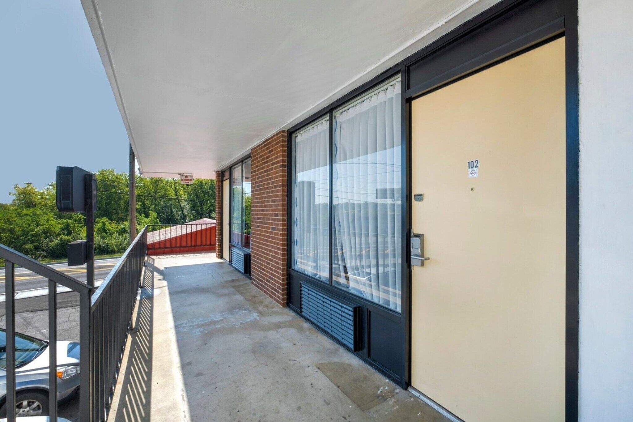 A balcony with a metal railing, a beige door with a number, and a brick wall.
