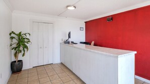 Une cuisine avec un plan de travail blanc, un mur rouge, une porte et une plante en pot.