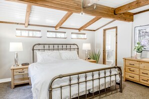 A bedroom with a metal bed frame, wooden headboard, bedside tables with lamps, a dresser, and a large mirror.
