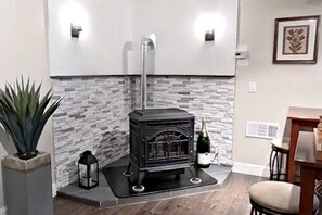 A wood-burning stove with a stone wall backdrop, a potted plant, and a small table with a chair.