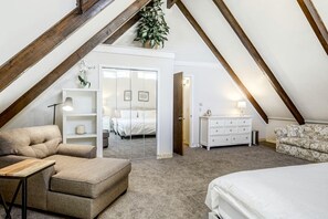 A bedroom with a loft-style ceiling, a bed, a sofa, a dresser, and a mirror.
