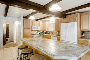A kitchen with wooden cabinets, a large island with stools, a white refrigerator, and a microwave.