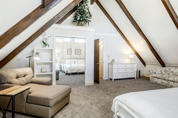 A bedroom with a loft-style ceiling, a bed, a sofa, a dresser, and a mirror.