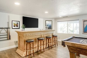 A bar area with a pool table and four stools, a television mounted on the wall, and framed artwork.
