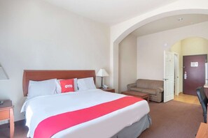 A hotel room with a bed, a chair, a desk, and an arched doorway. - Premium King Bed with Pull Out (Clute TX)