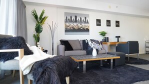Ett modernt vardagsrum med en soffa, ett soffbord och ett sidobord. Det finns en växt, en lampa och en inramad tavla på väggen.
