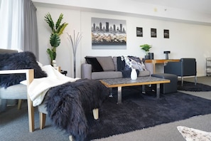 Un salon moderne avec un canapé, une table basse et une table d’appoint. On y trouve une plante, une lampe et un tableau encadré accroché au mur.