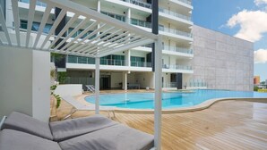 Ett område vid poolen med solstolar, en pool och en modern byggnad med balkonger.