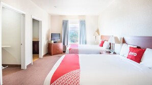 Une chambre d’hôtel avec deux lits, une télévision, un bureau et une fenêtre avec des rideaux.