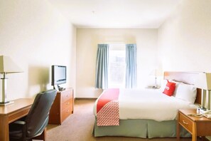 Ein Hotelzimmer mit Bett, Schreibtisch, Stuhl, Fernseher und einem Fenster mit Vorhängen.
