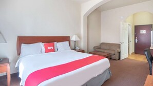 Ein Hotelzimmer mit Bett, Stuhl, Schreibtisch und einem rundbogigen Durchgang.