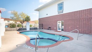 Ein Swimmingpool mit einer Ziegelmauer und einem weißen Gebäude im Hintergrund.
