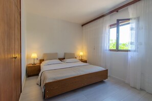 Ein Schlafzimmer mit einem Holzbett, zwei Nachttischlampen, einem Fenster mit durchscheinenden Vorhängen und einem Holzschrank.