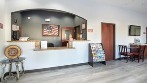 A reception area with a curved counter, an American flag, a framed picture, a small table with a decorative item, and a display board with brochures. - Premium 2 Queen Bed with Kitchenette (Clute TX)