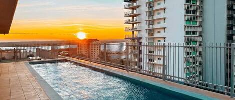 A swimming pool with a sunset view, surrounded by a high-rise building with balconies.
