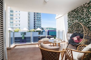 A balcony with wicker furniture, a glass table, and a view of buildings. - Charming | Rooftop Pool, CBD & Sunrise Balcony (Darwin City)